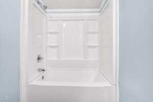 A white bathtub and shower combination with built-in shelves on three sides, chrome faucet and showerhead, and light blue walls.