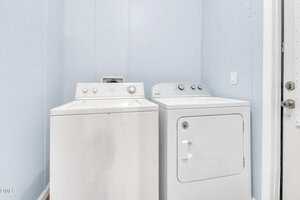 A white top-loading washing machine and a white front-loading dryer are positioned side by side in a small laundry room with light blue walls.