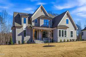 Two-story modern house with gray siding, large front porch, and multiple gables; new landscaping with a small tree and freshly laid sod in the front yard, under a clear blue sky.
