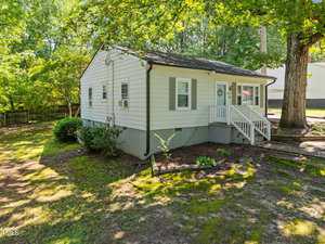 A small, single-story white house with gray shutters and a front porch sits under leafy trees at 860 Nelson Street in Henderson. There are shrubs and a small garden bed in the yard, and a fenced area is visible to the left.