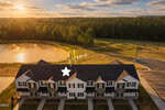 A row of white townhouses with black shutters is seen from above at sunset in Oxford, with a pond and forest behind. A star and "Home" mark one unit, highlighting 1103 Brookrun Drive.