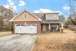 Located at 1180 Andrews Court in Creedmoor, this two-story brick and siding house features a double garage, a covered front porch with two chairs, and a large concrete driveway. The dry yard has patchy grass and is surrounded by trees under a partly cloudy sky.