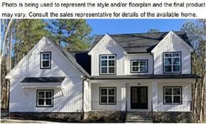 A two-story white house with black shutters and roof at 3907 Cedar Knolls Drive, Youngsville, features a stone foundation and multiple front-facing windows. Surrounded by leafless trees, the home appears newly constructed.