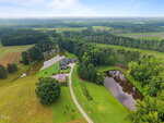 Aerial view of a rural property at 3700 Lark Farm Road, Franklinton, featuring a house and outbuilding between two ponds, surrounded by green lawns, trees, and open fields under a partly cloudy sky. A curved driveway leads to the house.