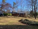 Charming single-story brick house at 314 Willowood Drive in Henderson, featuring white trim, a dark roof, and a spacious grassy yard with trees, shrubbery, and a pile of leaves under a clear blue sky.