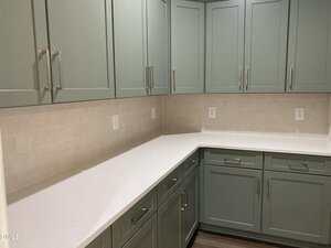 A kitchen corner with light green cabinets, white countertops, beige subway tile backsplash, multiple drawers, and several electrical outlets on the wall.