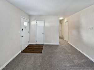 A small entryway with a white door, a closet, and a section of dark wood flooring next to light carpeted flooring. The hallway leads to multiple rooms with neutral-colored walls.