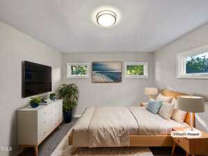 A modern, virtually staged bedroom with a light wood bed, neutral bedding, matching nightstands with lamps, a white dresser, a wall-mounted TV, potted plants, and artwork above the bed. Three small windows provide natural light.