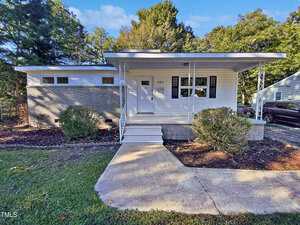 Charming single-story home at 205 N Chavis Street, Franklinton, featuring a blend of brick and white siding exterior, covered front porch with railings, concrete steps and walkway, plus shrubs in the front yard and trees in the background.