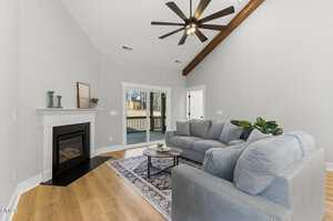 A modern living room with light gray walls, wood flooring, a gray sectional sofa, a round coffee table on a patterned rug, a fireplace with decor, and sliding glass doors leading to a deck.