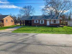 A single-story red brick house with white trim at 1808 S Clearview Drive, Henderson, features a covered carport and a well-maintained front lawn. Leafless trees and neighboring houses are visible in the background on this quiet residential street.