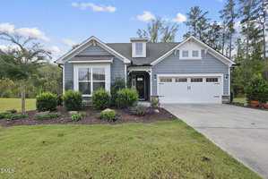 Charming single-story house at 40 Stormy Bluff Court, Youngsville, with light blue siding, white trim, large front windows, and a two-car garage. Features a landscaped front yard with shrubs and a concrete driveway leading to the street.