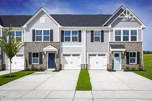 Two modern townhouses at 426 Moose Meadow Way in Youngsville feature white and gray siding, stone accents, blue front doors, attached garages, and small green lawns. A young tree is planted on the left side beneath the clear blue sky.