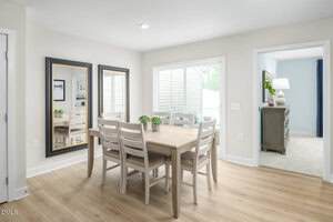 A dining area with a wooden table and six chairs, two large mirrors on the wall, sliding glass doors to the outside, and a view into an adjacent room with a dresser and lamp.