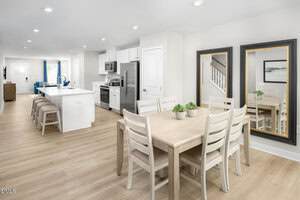 Open-concept kitchen and dining area with light wood floors, white cabinets, stainless steel appliances, a kitchen island with stools, and a dining table with six chairs. Two large mirrors are on the wall near the table.