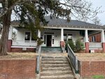 A charming single-story house at 431 Charles Street in Henderson features a covered front porch, white siding, and red brick accents. Concrete steps with metal railings lead up from the sidewalk to the home, surrounded by leafless trees and sparse grass.