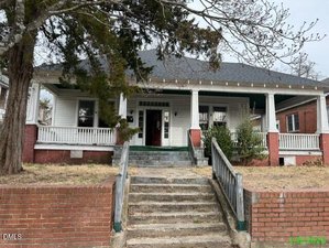 A charming single-story house at 431 Charles Street in Henderson features a covered front porch, white siding, and red brick accents. Concrete steps with metal railings lead up from the sidewalk to the home, surrounded by leafless trees and sparse grass.