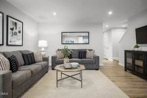 A modern living room with two gray sofas, a light area rug, a wooden coffee table with a plant and bowl, wall art, a floor lamp, a large mirror, a TV on a cabinet, and hardwood flooring.