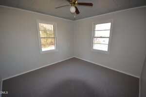 Empty room with light gray carpet, off-white walls, two windows, and a ceiling fan with a light fixture. The ceiling is painted a light blue color. Natural light enters through the windows.