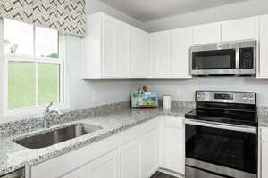 Modern kitchen with white cabinets, granite countertops, stainless steel oven and microwave, a sink under a window with patterned valance, and a small section of kitchen items on the counter.