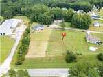 Aerial view of a grassy, rectangular plot at 35 Cotton Drive, Louisburg, bordered by roads and neighboring houses. A red marker pin is placed near the center of the plot. Trees and other homes surround the area.