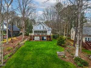 Situated at 651 Sagamore Drive in Louisburg, this two-story gray house with large windows and a wooden deck overlooks a spacious, well-maintained green lawn, surrounded by trees and neighboring homes on either side.