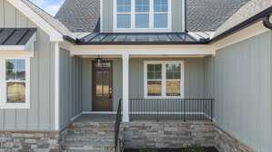A front porch of a house with gray vertical siding, stone accents, a brown door with a glass panel, black railing, steps leading to the entrance, and large windows above and beside the door.