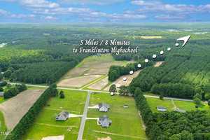 Aerial view of a rural neighborhood with houses, roads, fields, and forests; an arrow with text indicates that Franklinton High School is 5 miles or 8 minutes away in the direction shown.