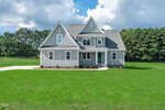 A two-story gray house with white trim sits on a large, well-manicured lawn at 105 Viola Lane, Franklinton. The home features multiple gables, a covered front porch, and is surrounded by trees under a partly cloudy sky.