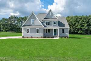 A two-story gray house with white trim sits on a large, well-manicured lawn at 105 Viola Lane, Franklinton. The home features multiple gables, a covered front porch, and is surrounded by trees under a partly cloudy sky.