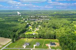 Aerial view of a rural neighborhood with several houses, surrounded by dense trees and open fields. Text and arrows indicate the area is 6 miles or 10 minutes from downtown Franklinton.
