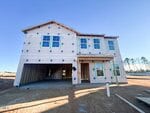 A two-story house at 12 Lotus Bend Way, Youngsville, is under construction, with exterior walls covered in insulation wrap, exposed garage framing, and no landscaping or driveway; construction materials and dirt are visible in the foreground.
