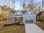 This two-story suburban house at 952 Sagamore Drive, Louisburg features blue siding, beige brick, a covered front porch, and a two-car garage. A sloped driveway leads up to the home, which is surrounded by trees and a spacious lawn.
