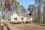 A single-story beige house with a brown roof, white trim, and brick steps sits at 303 S Stratford Drive in Henderson, surrounded by tall trees and fallen leaves. A driveway runs along the right side under a clear blue sky.