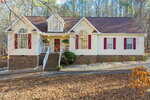 Charming single-story home at 2036 Landmark Drive in Franklinton features a brick foundation, light-colored siding, red shutters, and a dark brown roof. Steps lead to a covered front porch, with trees and fallen leaves accenting the yard.