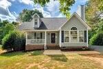 A light gray house with white trim at 70 Grist Mill Drive, Franklinton features a front porch with white railings, dark shutters, an arched window, black front door, inviting shrubs by the entrance, and a driveway on the right.
