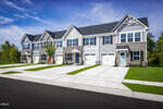 Row of modern two-story townhomes at 1005 Knickerbocker Lane in Youngsville, featuring attached garages, stone and siding exteriors, neatly trimmed lawns, and a wide driveway under a clear blue sky.