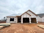 A single-story house under construction at 9 Bee Balm Court in Youngsville, with exterior walls wrapped in weather-resistant material, an open garage, plywood sheets, and lumber stacked on bare earth. The sky is overcast.