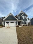 A two-story modern house with blue-gray siding, white trim, and a double garage sits at 185 Sugar Pine Drive in Franklinton. It features a large driveway, gabled roof, for-sale sign, and is surrounded by lawn and trees under a partly cloudy sky.