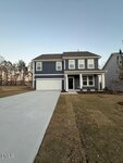 Charming two-story blue house with white trim at 265 Sugar Pine Drive, Franklinton. Enjoy a front porch, attached double garage, freshly laid sod, and a wide driveway. Trees line the background under a clear sky.
