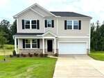 Charming two-story beige house at 135 Cordoba Drive in Franklinton, featuring black shutters, a covered front porch, white garage door, well-maintained lawn, and mature trees and greenery in the background.