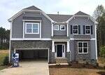 Two-story modern house at 115 Guardian Street in Youngsville with gray siding, stone accents, double garage, white trim, blue shutters, and a blue front door. The landscaped front yard is surrounded by trees.
