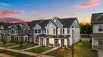 Row of modern two-story townhomes with gray and white exteriors, manicured lawns, and a sunset sky in the background; a streetlamp stands near the sidewalk in front at 945 Alma Railway Drive in Wake Forest.