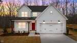 A modern two-story white house at 650 Husketh Road, Youngsville, featuring a red front door, double garage, and outdoor lights. The newly landscaped yard is framed by leafless trees in the background at sunset.