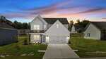 A modern two-story white house with a double garage, front porch, and well-maintained yard at 25 Malbec Way in Youngsville, set in a suburban neighborhood at sunset with a colorful sky.