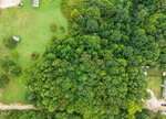 Aerial view of a dense green forest near Franklinton, bordered by grassy open fields and a few scattered small buildings. A dirt road, 0 W River Road, runs along the bottom edge of the image.