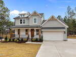 Modern two-story house at 30 Vino Trail, Franklinton, with gray siding, white trim, covered front porch, wooden accents, and a double garage. The home features a landscaped yard and sits beside a wooded area under a clear blue sky.