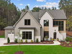 Two-story modern house with gray and white exterior, large windows, attached garage on the left, landscaped front yard with grass, small plants, and curved walkway, surrounded by tall trees and blue sky.