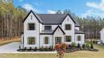 A modern two-story house at 190 Cherry Bark Drive, Youngsville, features white siding, black trim, and a dark roof, surrounded by a landscaped yard and tall pine trees under a blue sky with scattered clouds.
