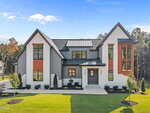 Modern two-story house at 170 Cherry Bark Drive in Youngsville with large windows, gray and white exterior, wood accents, black roof, and a neatly landscaped yard on a sunny day under a blue sky.